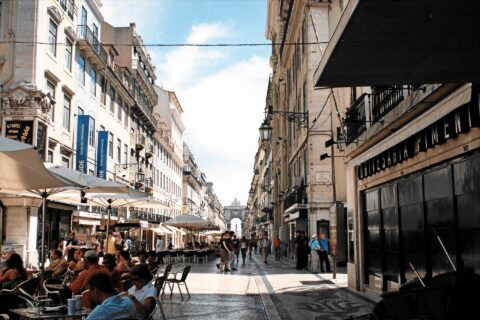 Visitors and cafe tables line Lisbon’s Rua Augusta, with patterned paving leading toward the triumphal arch.