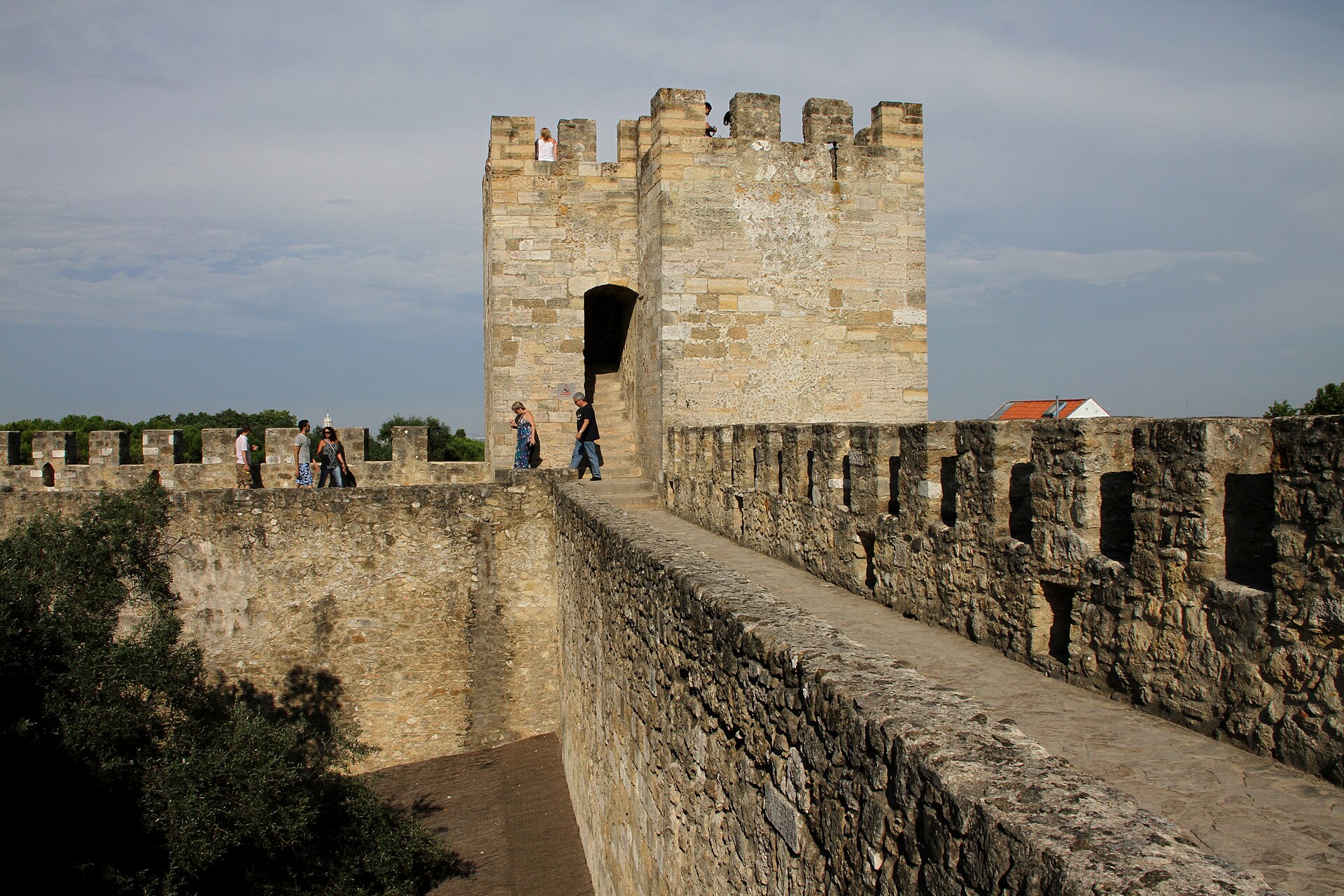 Visitors follow a stone rampart toward a square crenellated tower at São Jorge Castle in Lisbon.