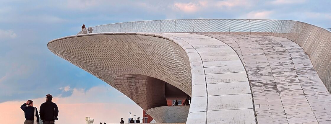 Visitors stand beside MAAT’s sweeping ceramic-clad roof in Lisbon, with more people visible along the curved rooftop railing.