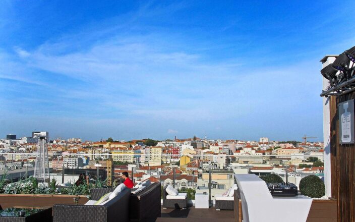 White counters and wicker lounge seats overlook Lisbon rooftops from Level Eight rooftop bar on a clear day.