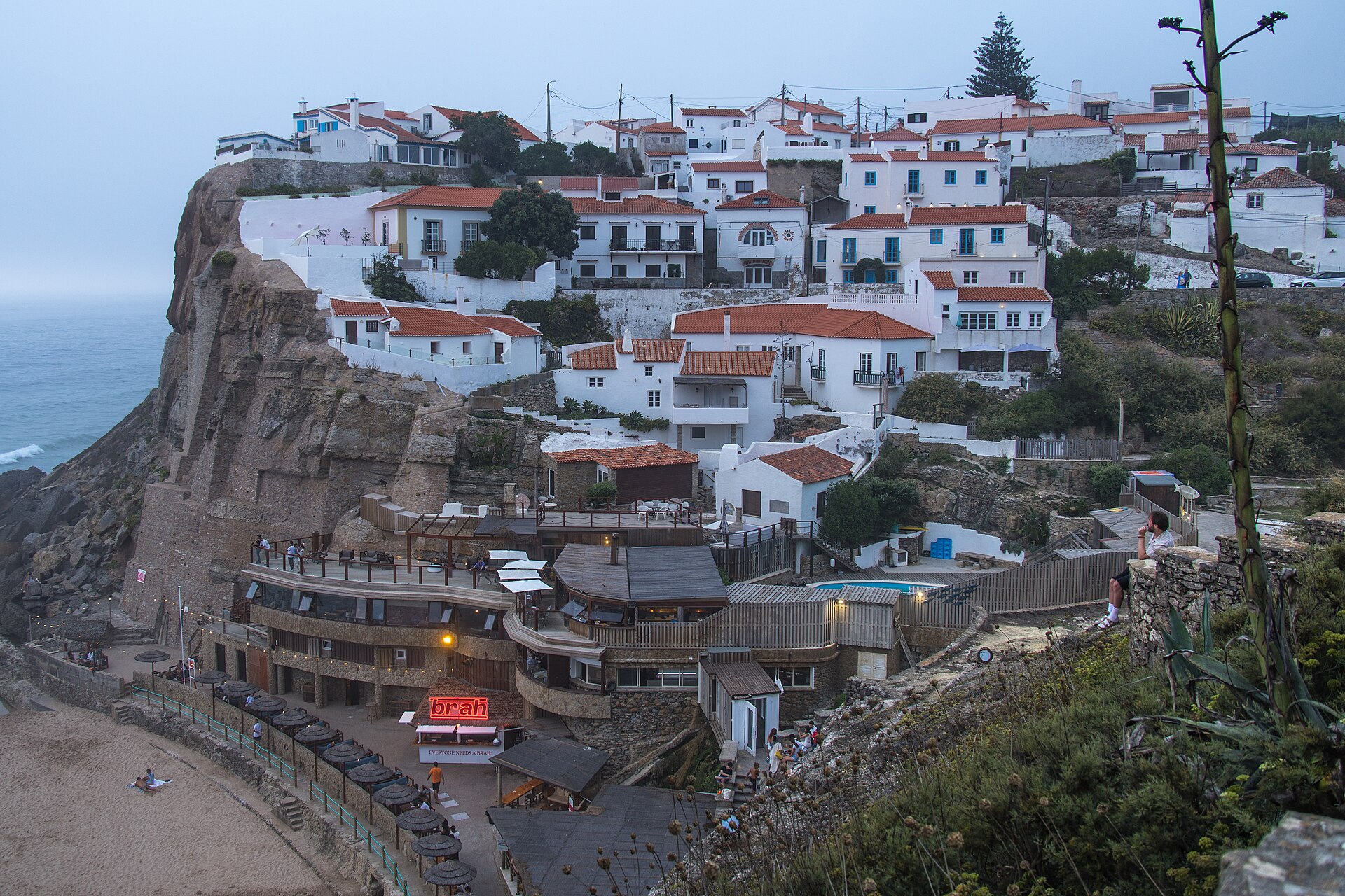 Whitewashed houses cascade down the cliff at Azenhas do Mar, above beachfront terraces beside the Atlantic Ocean.