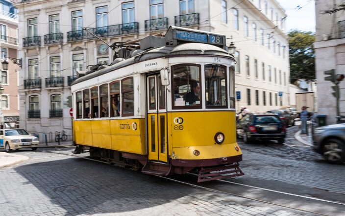 Yellow Carris Tram 28 turns along cobbled tracks in Lisbon, passing balconied buildings with passengers aboard.